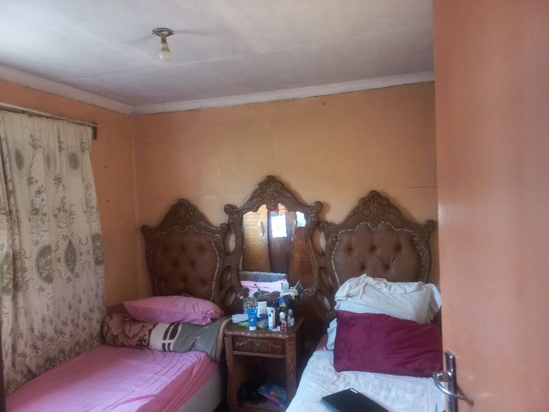 A bedroom featuring a central vanity unit between two beds, with plain ceiling and standard window treatments.