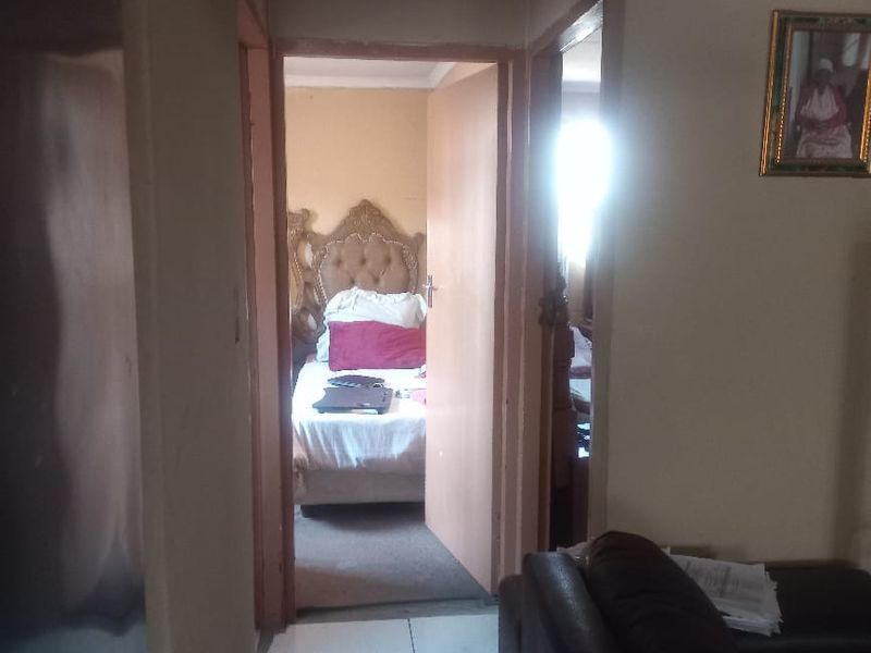 A view from a living area looking through a hallway into a bedroom, featuring tiled flooring and a timber-paneled ceiling.