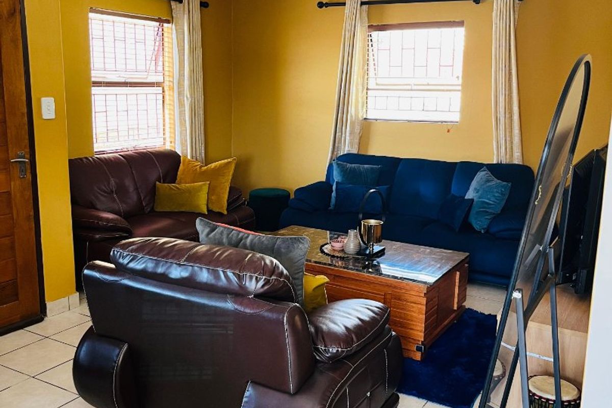 A living room featuring ceramic floor tiles, mustard-colored walls, and windows fitted with security bars.