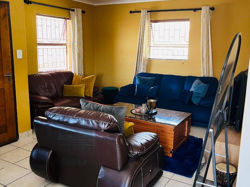 A living room featuring ceramic floor tiles, mustard-colored walls, and windows fitted with security bars.