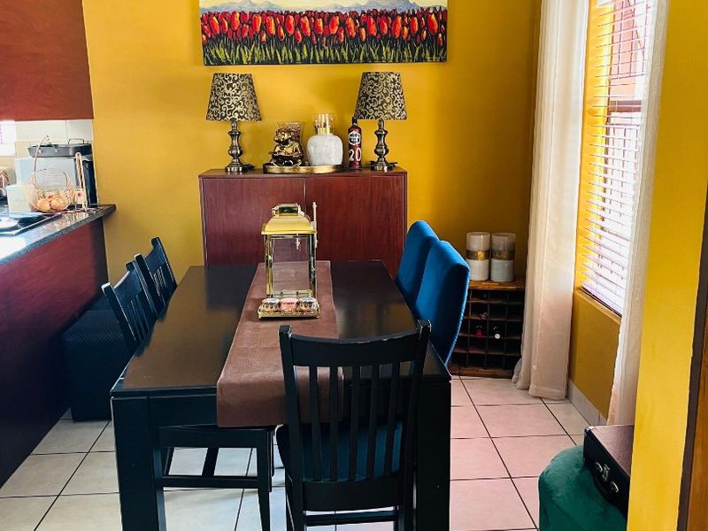 A dining area featuring tiled flooring and a breakfast bar, adjacent to the kitchen with natural light provided by a window with venetian blinds.