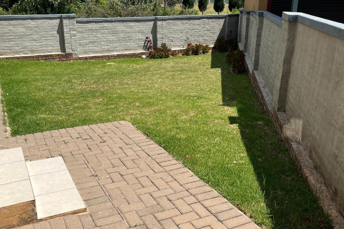 A private rear garden featuring a paved patio area, a well-maintained lawn, and secure boundary walls.