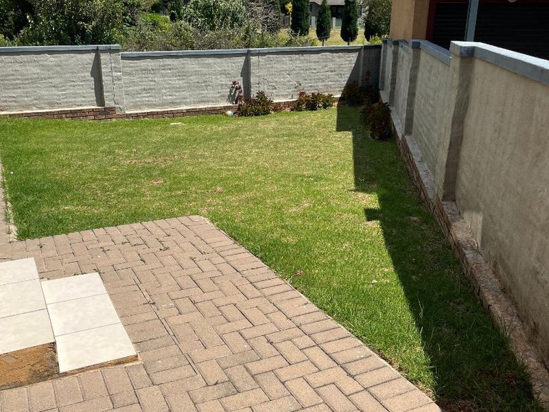 A private rear garden featuring a paved patio area, a well-maintained lawn, and secure boundary walls.