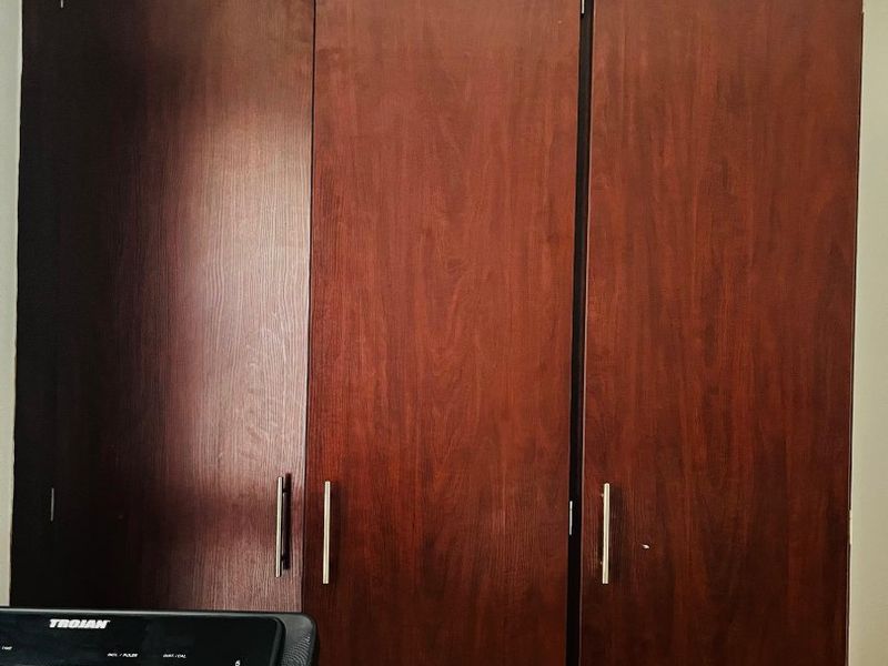 A bedroom featuring dark wood-finish built-in cupboards with modern metal handles.