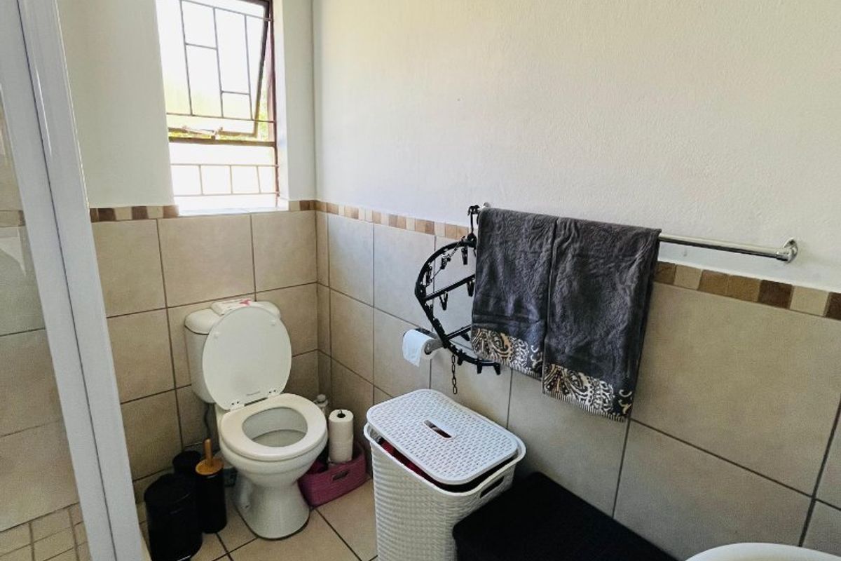 A functional bathroom featuring a toilet, shower enclosure, and tiled finishes with a window providing natural light.
