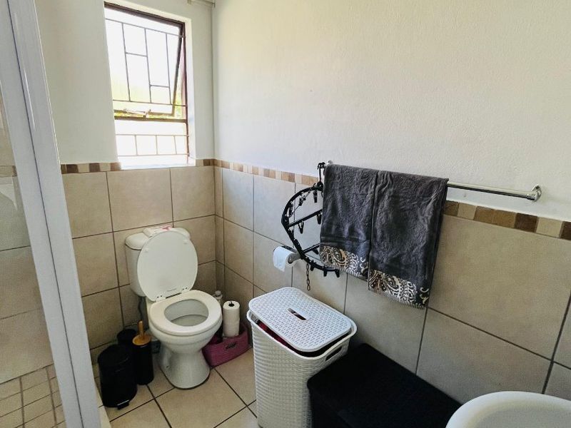 A functional bathroom featuring a toilet, shower enclosure, and tiled finishes with a window providing natural light.