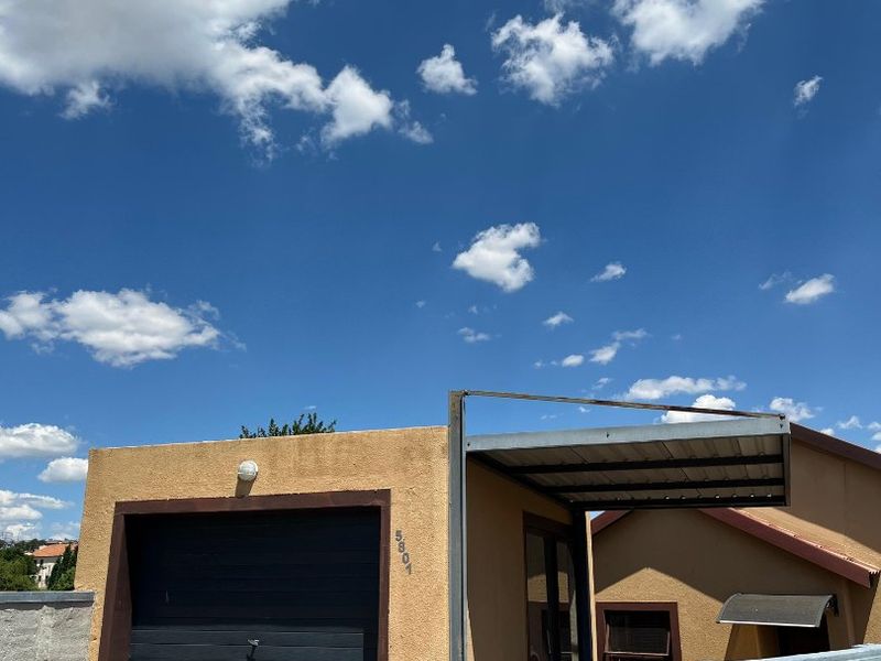 Front exterior view of the property featuring a single garage, attached carport, paved driveway, and secure boundary walling.