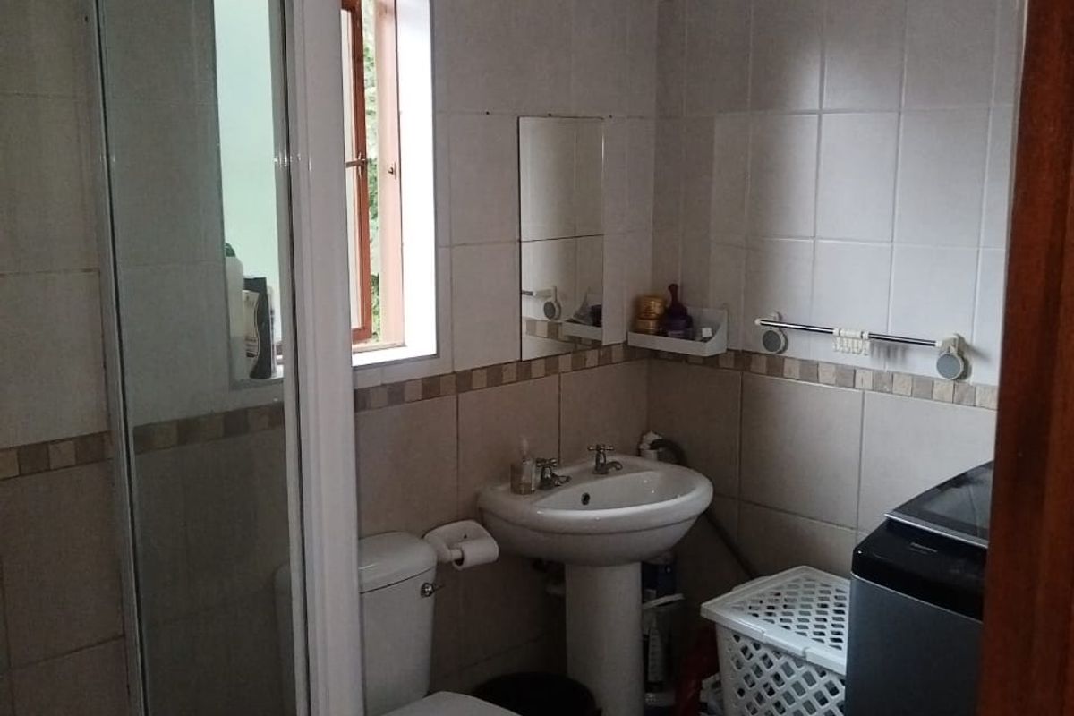 A compact bathroom featuring a pedestal basin, toilet, and shower enclosure with tiled walls and flooring, requiring some maintenance and cosmetic updates.