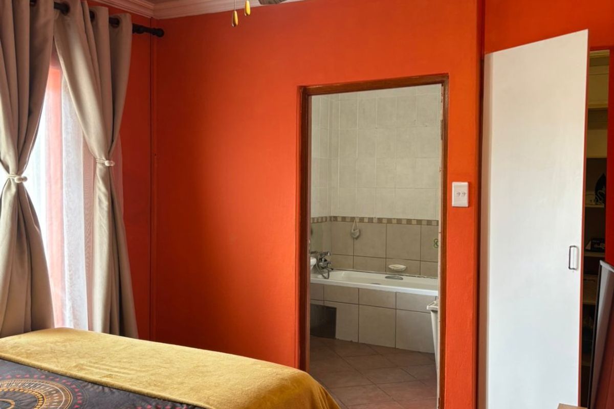 A bedroom featuring a ceiling fan, crown molding, and tiled flooring, with an adjoining en-suite bathroom and built-in closet access.