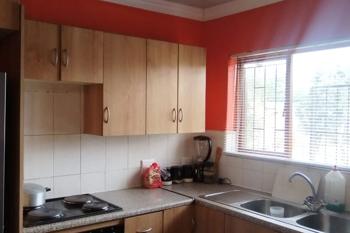 A functional kitchen featuring laminate cabinetry, built-in oven, electric hob, and a double bowl stainless steel sink with tiled splashback.