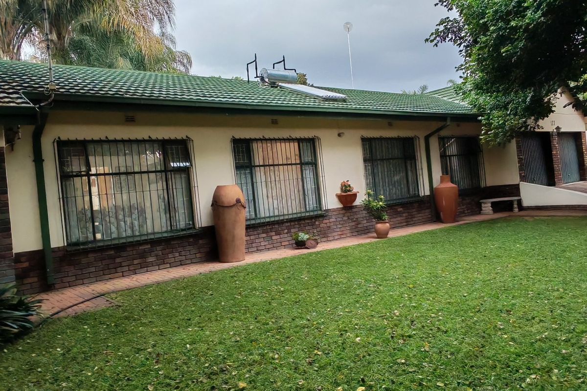 Rear view of the house featuring a tiled roof, solar water heater, brick exterior walls, and a paved walkway leading along the garden.