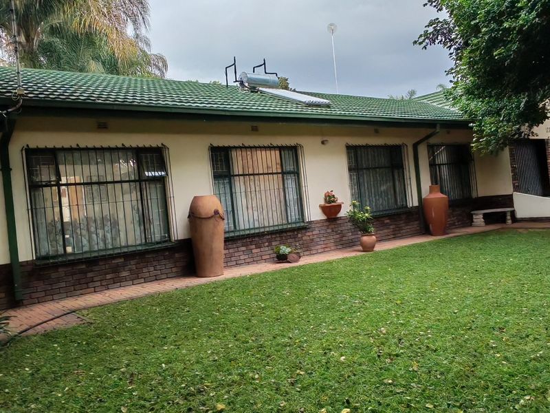Rear view of the house featuring a tiled roof, solar water heater, brick exterior walls, and a paved walkway leading along the garden.