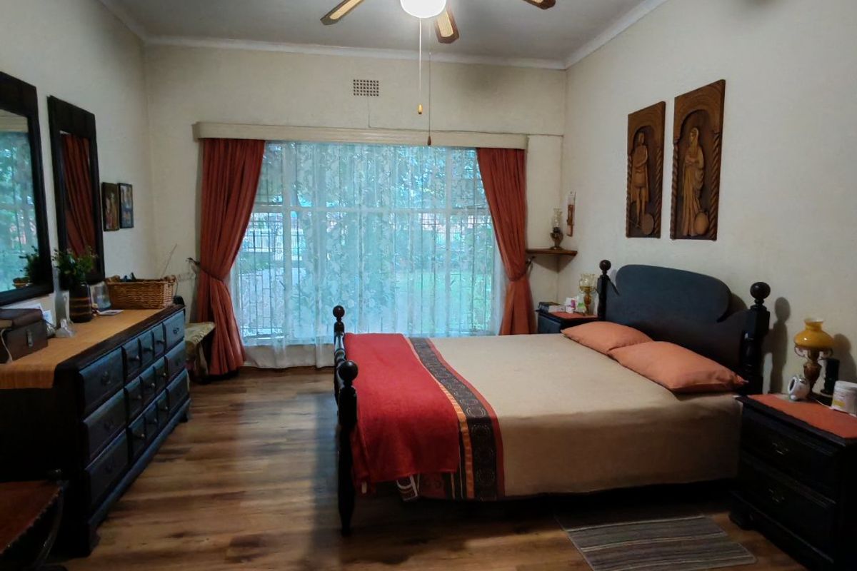 A spacious bedroom featuring laminate flooring, a central ceiling fan, and large windows with curtain rails, offering a comfortable and functional living space.