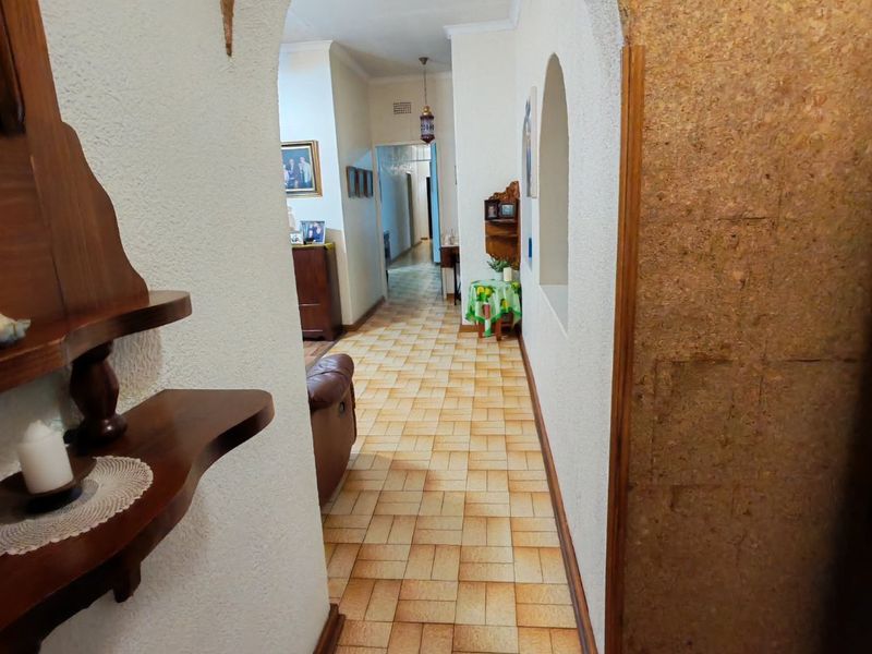 A traditional hallway featuring an arched entryway, textured walls with cork paneling, and durable ceramic tile flooring leading into the home.