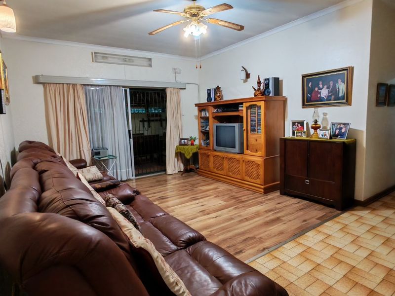 A living room featuring a mix of laminate and tiled flooring, a ceiling fan, and a sliding glass door leading to an outdoor area.