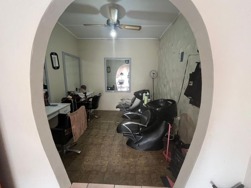 A functional utility space currently utilized as a salon, featuring tiled flooring, a ceiling fan, and built-in vanity mirrors.