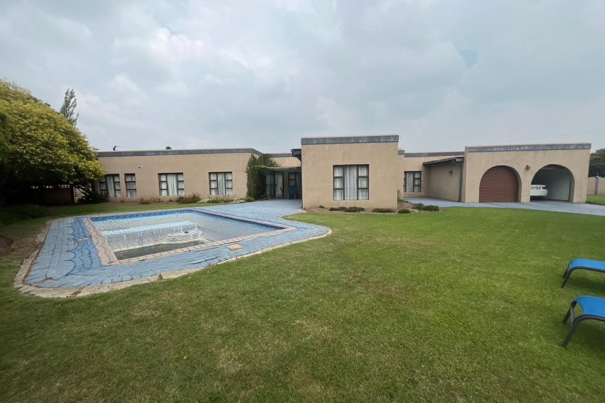 Rear view of the property featuring a swimming pool with a safety cover, expansive lawn, and an integrated arched garage.