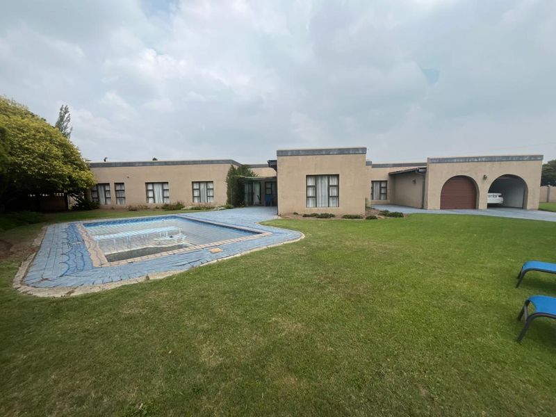 Rear view of the property featuring a swimming pool with a safety cover, expansive lawn, and an integrated arched garage.