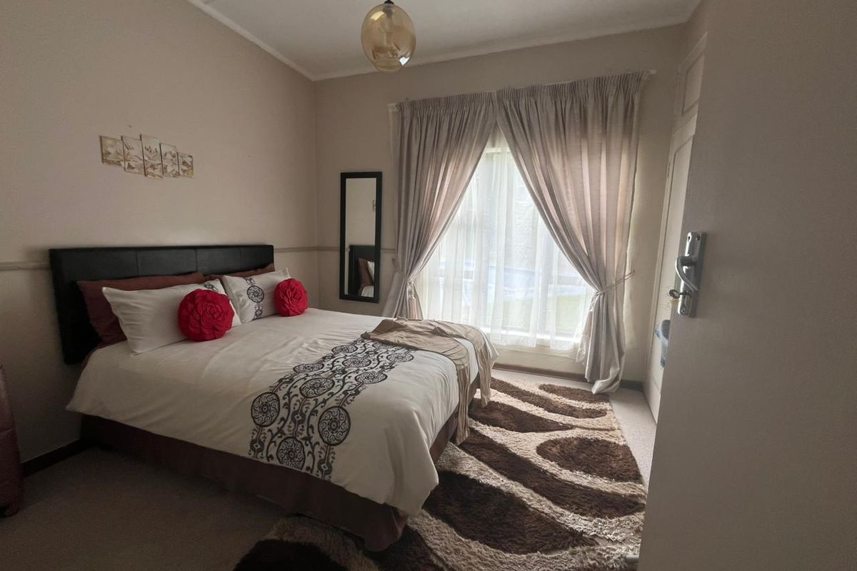 A well-lit bedroom featuring neutral wall tones, a large window with curtain treatments, and a central pendant light fixture.