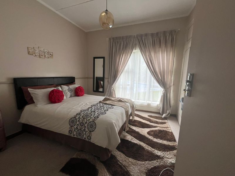 A well-lit bedroom featuring neutral wall tones, a large window with curtain treatments, and a central pendant light fixture.