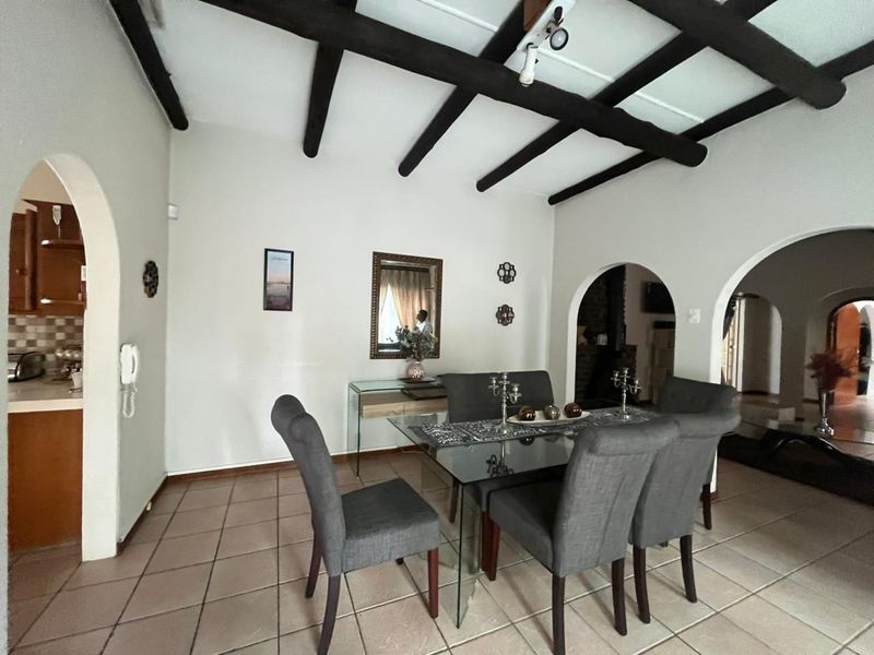 Dining room featuring exposed timber ceiling beams, ceramic floor tiles, and arched architectural transitions to adjacent living and kitchen areas.