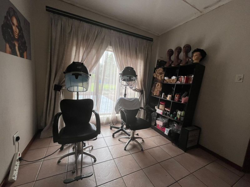 A utility room currently utilized as a salon space, featuring tiled flooring and a large sliding glass door with curtain track.