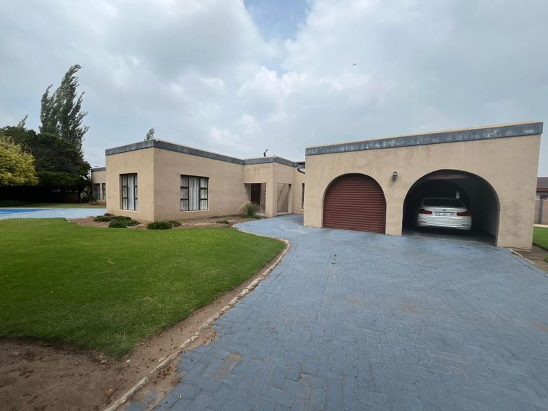 Front elevation of a single-story residence featuring a paved driveway, arched garage entrance, and well-maintained lawn area.