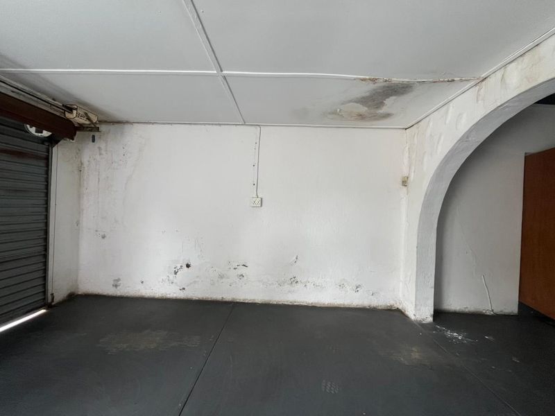An empty garage space featuring a roller shutter door, arched architectural detail, and visible signs of moisture damage on the ceiling and walls.