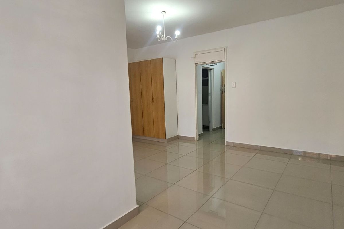 A spacious, empty bedroom featuring neutral tiled flooring and built-in wooden cupboards, offering a clean and versatile living space.