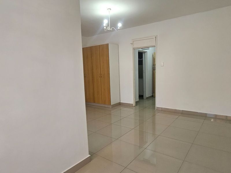 A spacious, empty bedroom featuring neutral tiled flooring and built-in wooden cupboards, offering a clean and versatile living space.