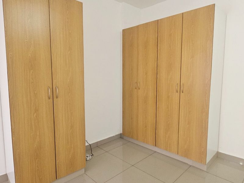 A clean, empty bedroom featuring light wood-finish built-in wardrobes and neutral tiled flooring, offering a bright and versatile living space.