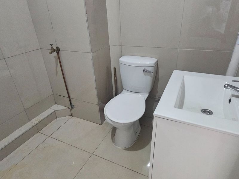 A compact bathroom featuring tiled surfaces, a standard toilet, and a vanity basin with exposed plumbing.