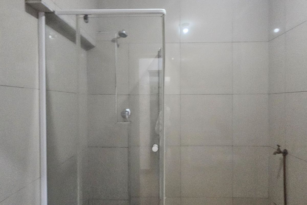 A functional bathroom featuring a glass-enclosed shower and neutral ceramic wall tiling throughout.