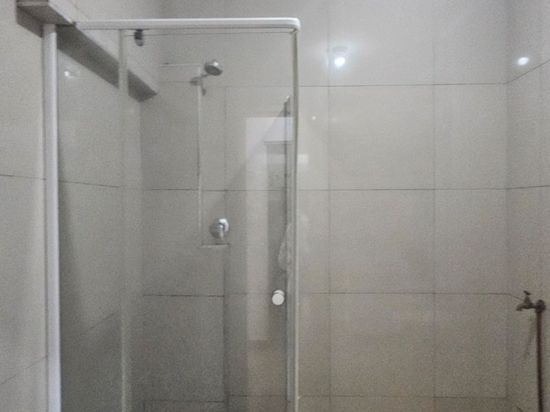 A functional bathroom featuring a glass-enclosed shower and neutral ceramic wall tiling throughout.