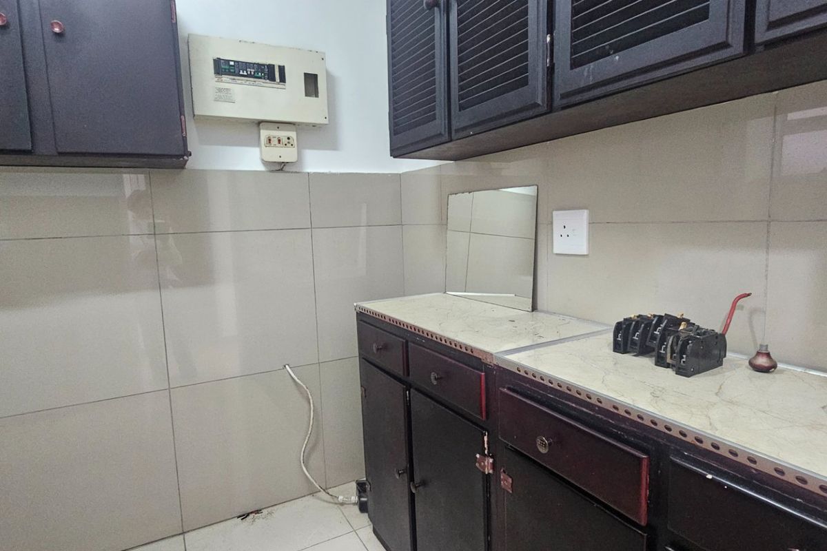 A dated kitchen area featuring dark built-in cabinetry, tiled splashbacks, and a laminate countertop, requiring cosmetic updates to improve its overall aesthetic appeal.