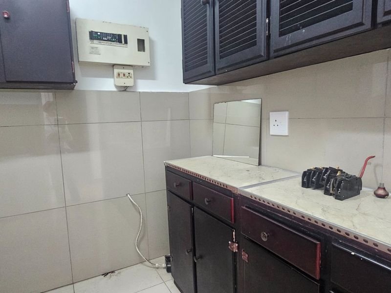 A dated kitchen area featuring dark built-in cabinetry, tiled splashbacks, and a laminate countertop, requiring cosmetic updates to improve its overall aesthetic appeal.