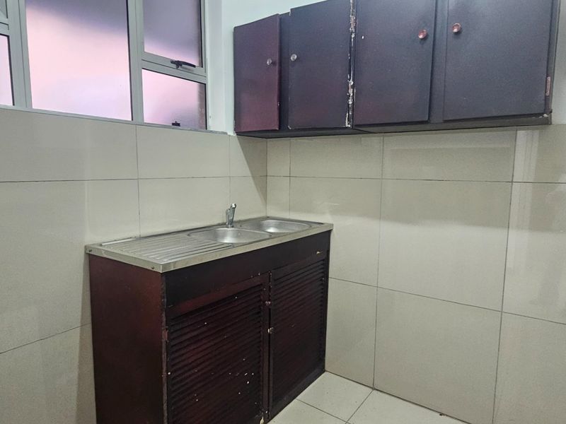 A functional scullery area featuring tiled walls, built-in cabinetry, and a stainless steel sink, providing a practical utility space.