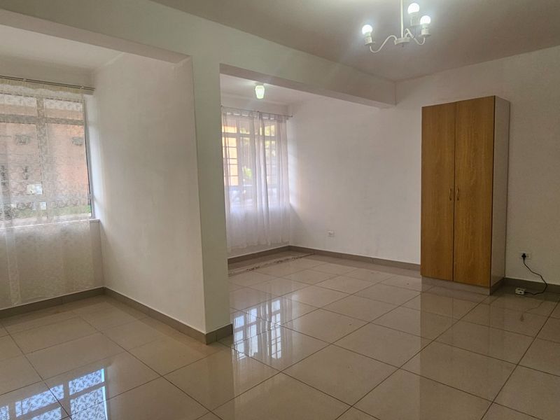Spacious open-plan living area featuring neutral tiled flooring, large windows for natural light, and built-in storage cupboards.