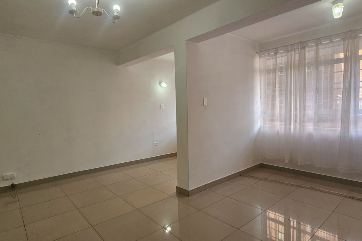 An empty, open-plan living area featuring neutral ceramic floor tiles, ample natural light, and clean white walls ready for personalization.