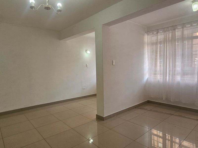 An empty, open-plan living area featuring neutral ceramic floor tiles, ample natural light, and clean white walls ready for personalization.