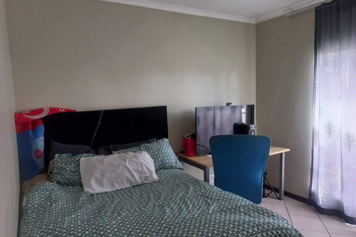 A standard bedroom featuring tiled flooring, neutral wall paint, and a window with curtain tracks.