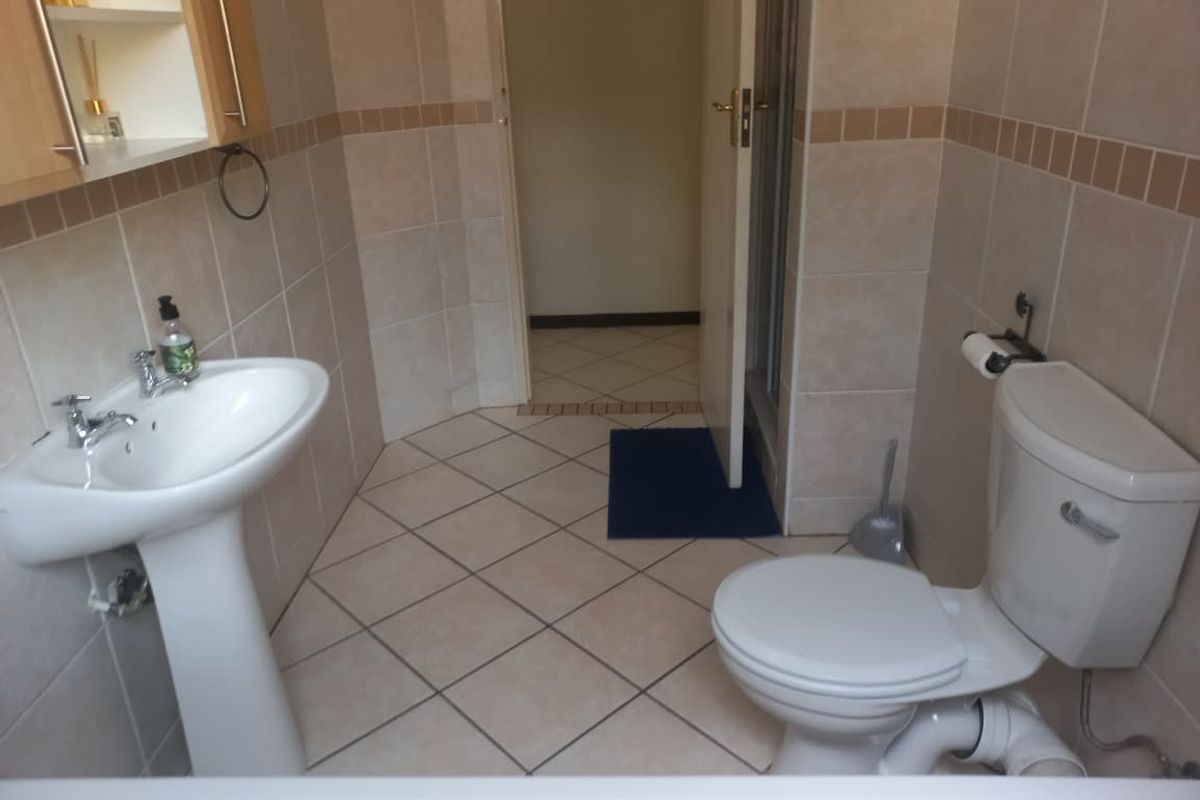 A functional bathroom featuring a pedestal basin, toilet, and tiled walls and flooring, providing a practical layout for daily use.