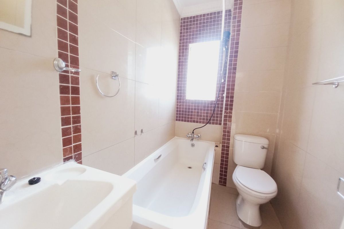 A functional bathroom featuring a bathtub, toilet, and vanity basin with neutral wall tiles and decorative mosaic accents.