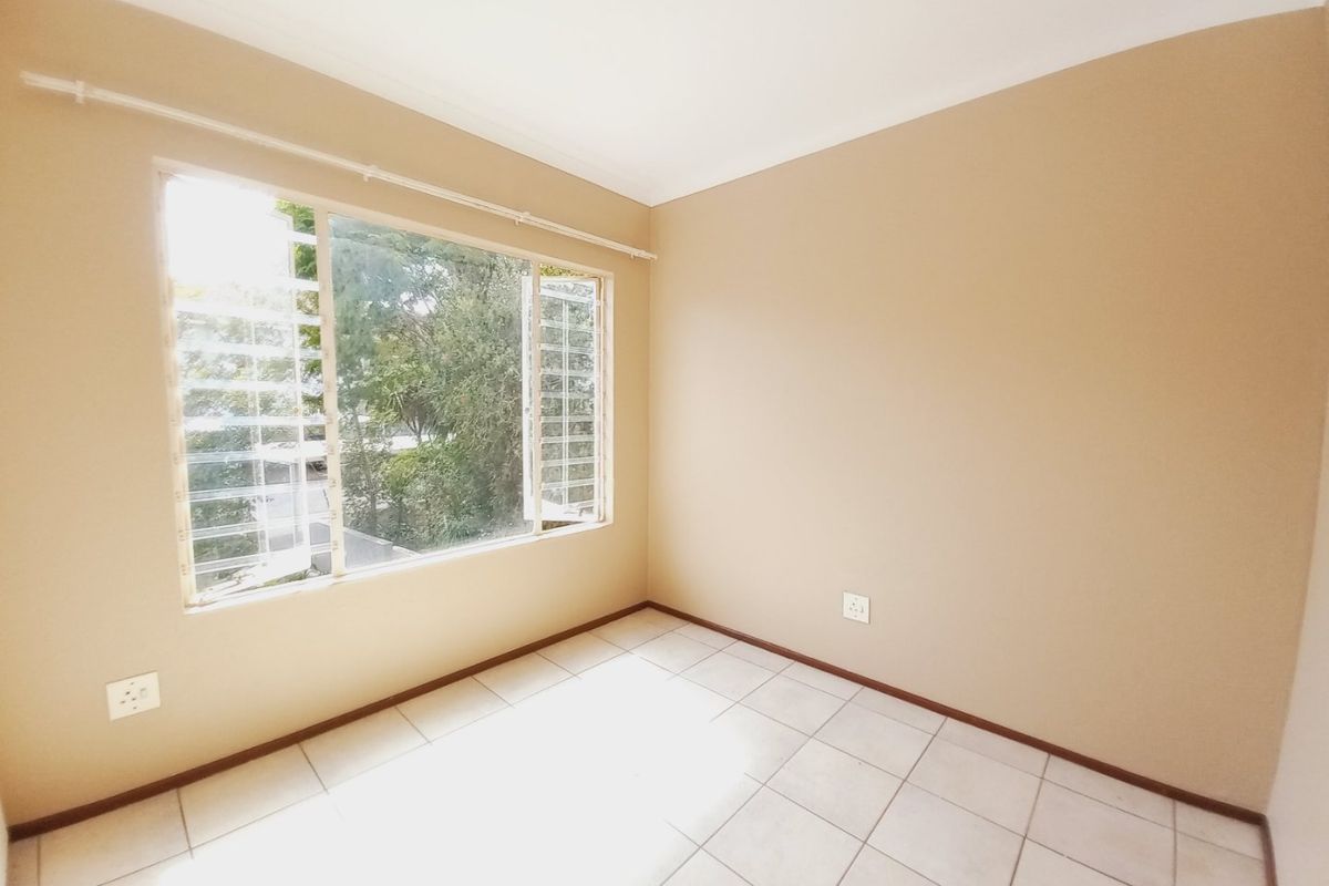 A bright, empty bedroom featuring neutral wall paint, tiled flooring, and louvered windows with security bars.