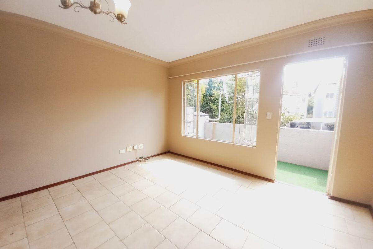A bright, empty living room featuring neutral tiled flooring, a ceiling light fixture, and direct access to an outdoor balcony area.
