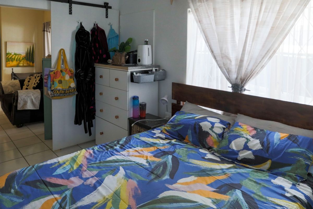 A functional bedroom featuring a window with security bars and a sliding door entrance, providing a comfortable and practical living space.