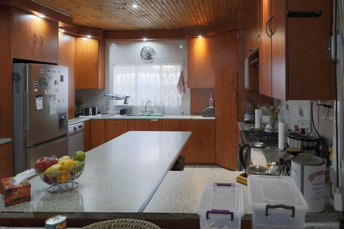 A functional kitchen featuring extensive timber cabinetry, laminate countertops, a gas hob, and a distinctive timber-clad ceiling with integrated lighting.