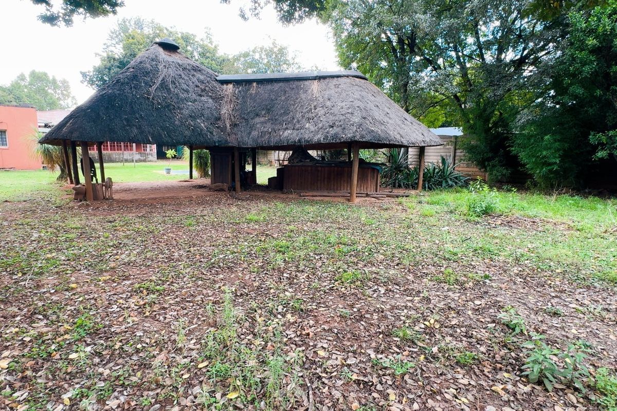 A spacious rear garden featuring a traditional thatch roof lapa with a built-in bar area, set within a large, mature outdoor space.