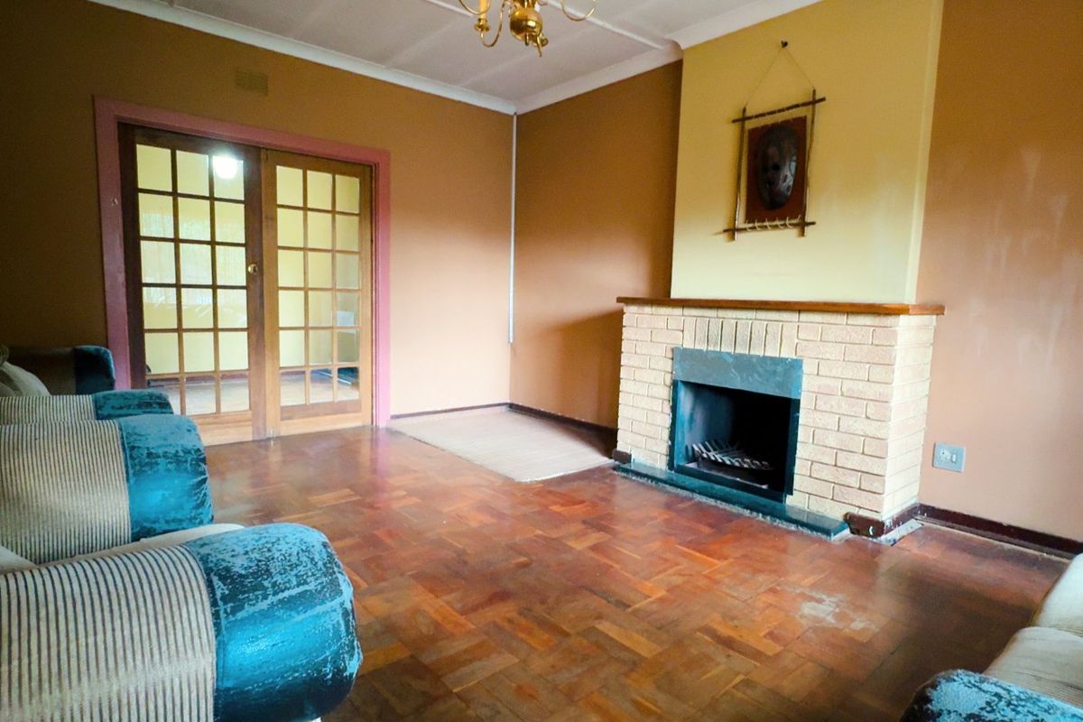 Living room featuring a brick fireplace, parquet flooring, and classic french doors, offering a traditional layout with potential for modernization.