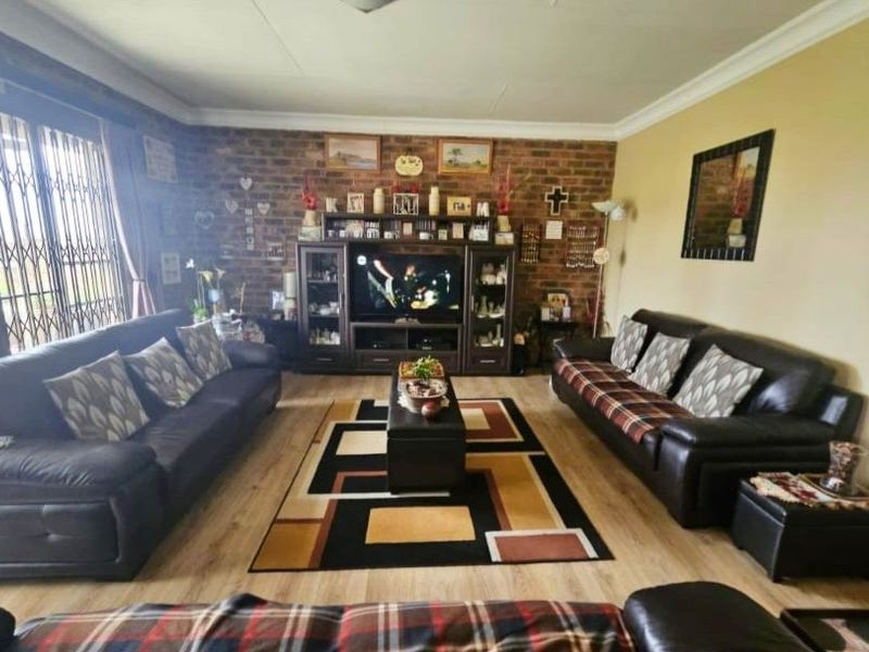 Spacious living room featuring an exposed brick feature wall, laminate flooring, and large sliding glass doors with security gates for natural light.